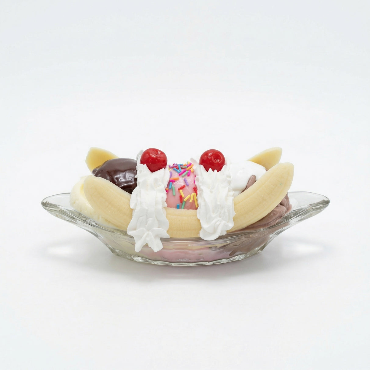 Realistic faux banana split with chocolate, vanilla and strawberry scoops in glass dish decor
