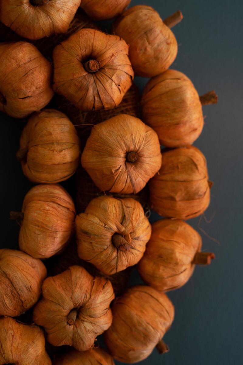 Orange faux pumpkin wreath shown on a light background