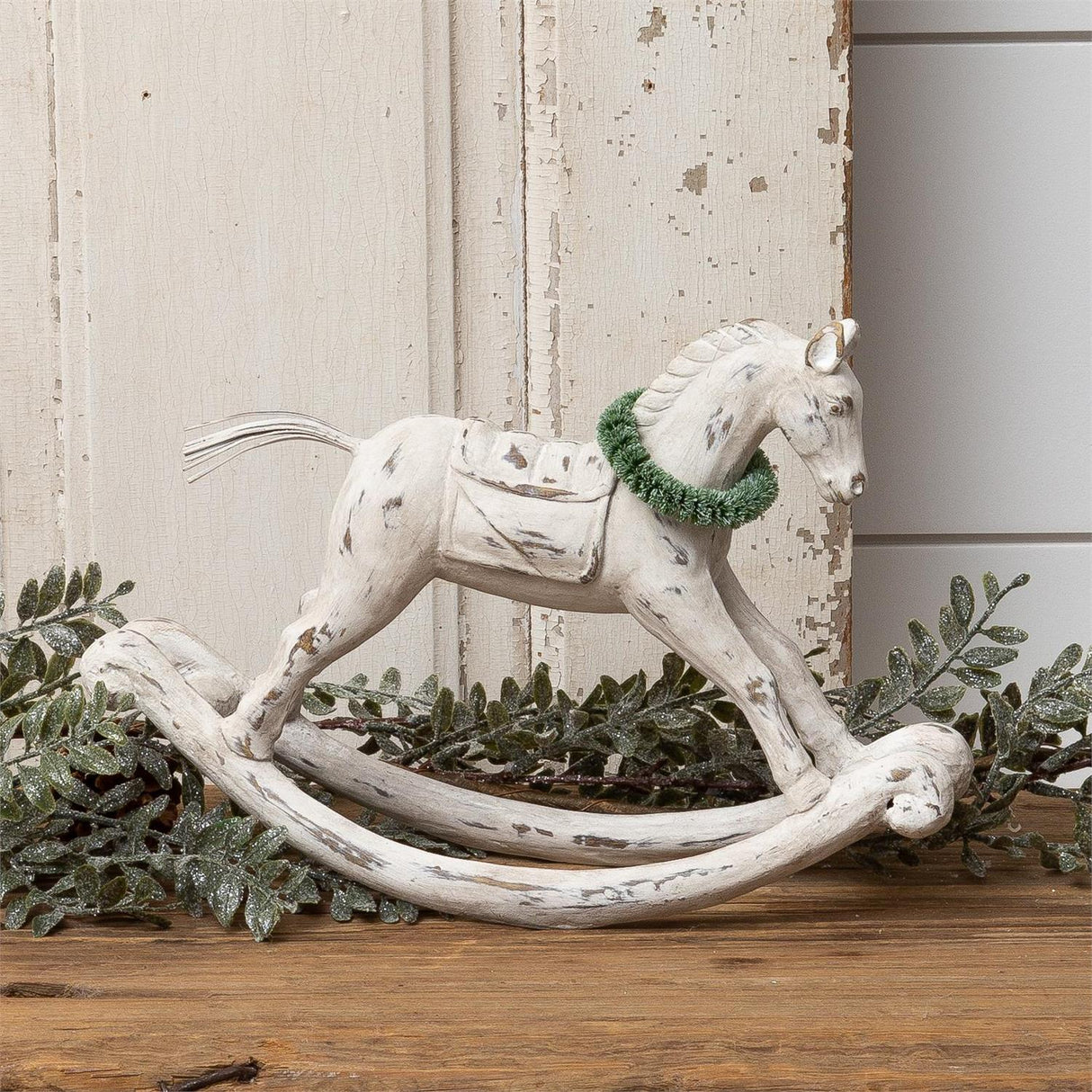 Distressed white rocking horse figurine with a green wreath around its neck.