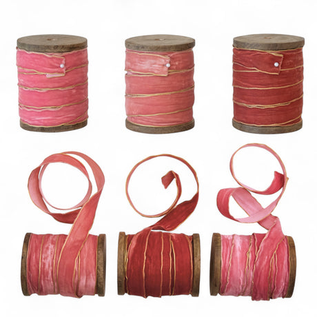 Three velvet ribbons with metallic edges on wooden spools, in varying shades of pink and red