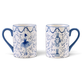 Opposite sides of a white ceramic mug showing blue ballerina and nutcracker illustrations with leafy branches, stars, bow garlands, and a blue handle