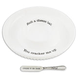 White ceramic cheese ball dish with funny text and a silver spreader that says Spread it on thick