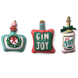 Three Christmas bottle shaped pillows featuring a teal wreath design, red Gin and Joy bottle, and Be Merry bottle with a green bow