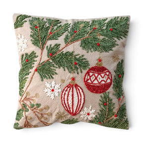 Square cotton Christmas pillow with embroidered green pine boughs, red and white ornaments, white snowflakes, and gold accents