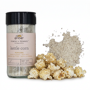 Finch + Fennel Kettle Corn Popcorn Seasoning in a clear jar with a black lid and pink label beside seasoned popcorn