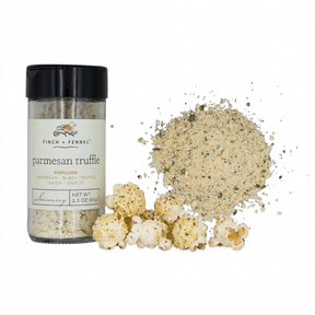 Finch + Fennel Parmesan Truffle Popcorn Seasoning in a clear jar with a black lid beside a sprinkle of seasoning