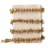 Slender gold glitter faux boxwood garland with small leaves, arranged in loose rows across an ivory background.