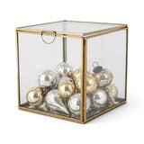 Small cube-shaped glass display box with a gold-tone metal frame and hinged glass lid