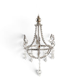 Silver metal chandelier ornament with curved scrollwork, clear acrylic jewels, and dangling faceted pendants.