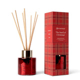 The Smell of Christmas mini reed diffuser in a red metallic glass bottle with a gold-tone collar, natural reeds, and red plaid gift box