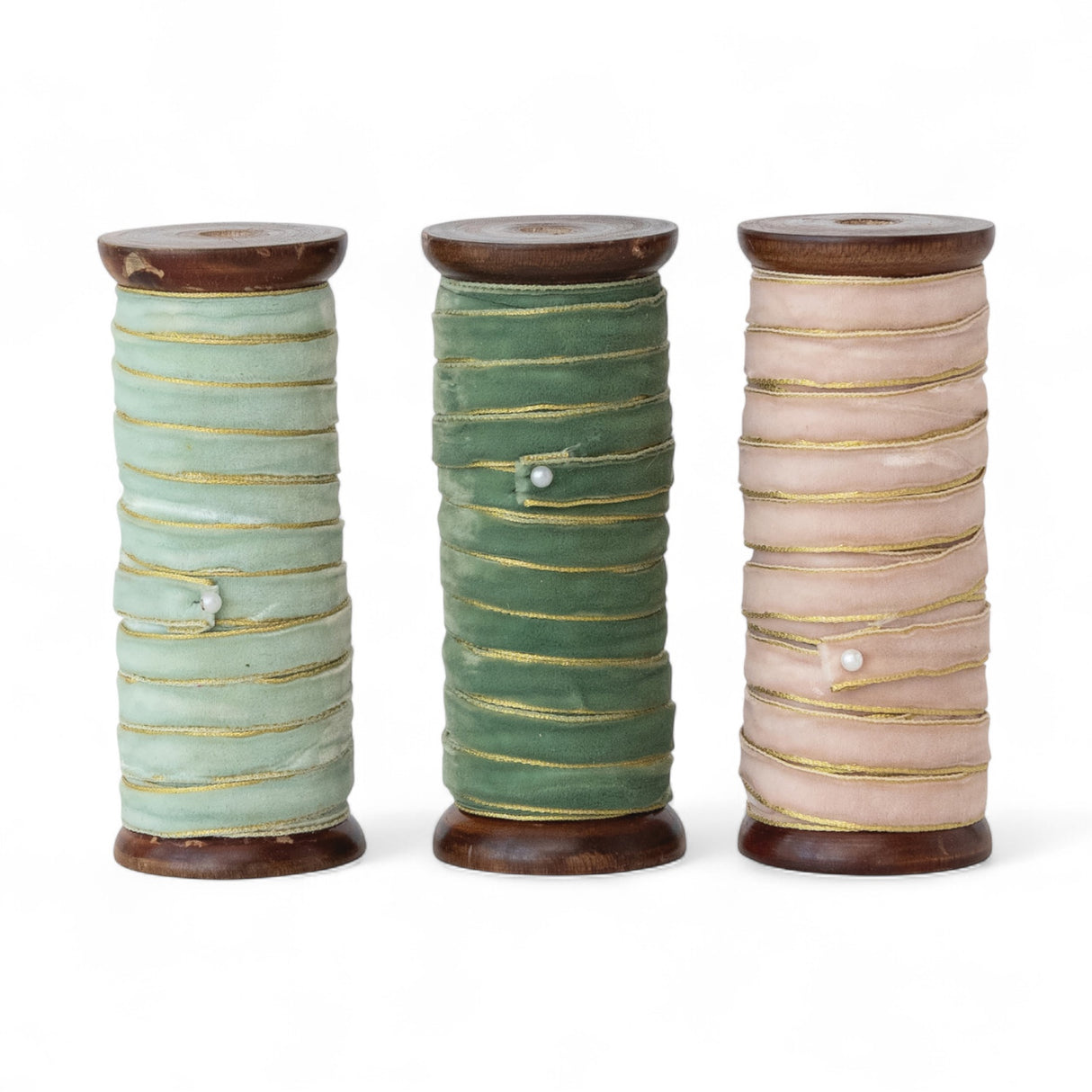 Three velvet ribbons with gold edges on wooden spools in mint, forest green, and blush pink