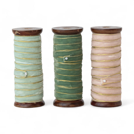 Three velvet ribbons with gold edges on wooden spools in mint, forest green, and blush pink