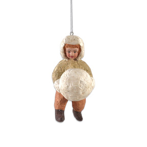 Vintage reproduction paper mache boy ornament wearing a cream winter hat, peach trousers, and dark boots while holding a large white snowball