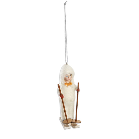 Vintage reproduction child skiing ornament in a cream hooded outfit with red mittens, a golden bow, skis, and brown ski poles