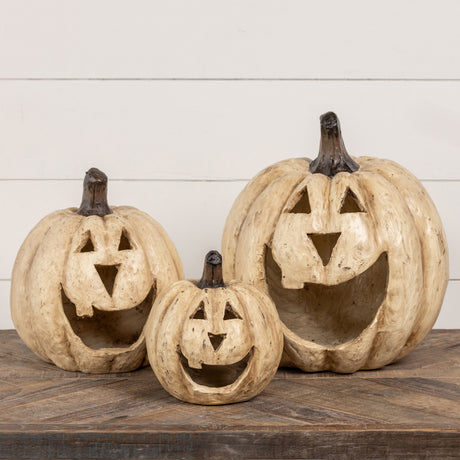 A set of three beige resin mache pumpkins with big mouth designs, displayed on a wooden surface against a white background.