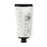 ILLUME Winter White Demi Hand Cream in a cream 3 fl oz tube with pale blue-green botanical illustrations, gold lettering, and a black cap